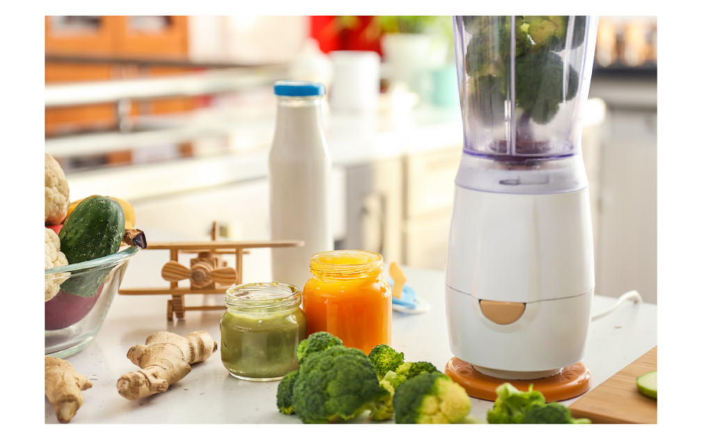 Baby food preparation setup with a blender containing broccoli, jars of green and orange purees, fresh vegetables, ginger root, and a bottle of milk on a kitchen counter.