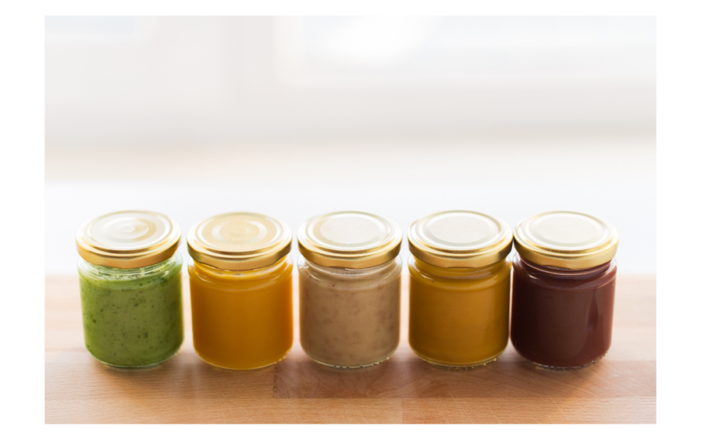 Glass storage jars filled with colorful homemade baby food, representing fresh and nutritious meal options for babies, displayed on a wooden surface.