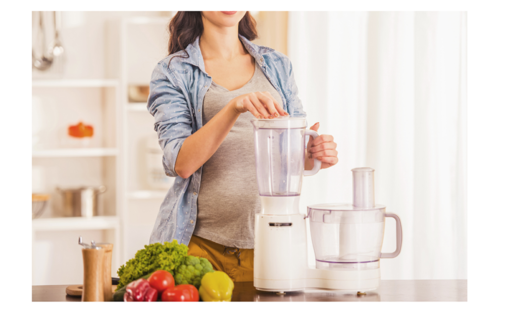 A woman preparing food with a food processor, featuring fresh produce on the counter, emphasizing healthy meal preparation in a home kitchen.